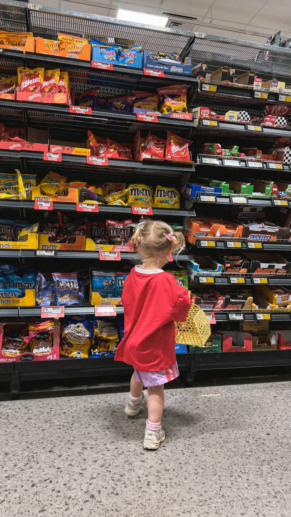 Child in a red shirt standing in front of a grocery store aisle with snacks.