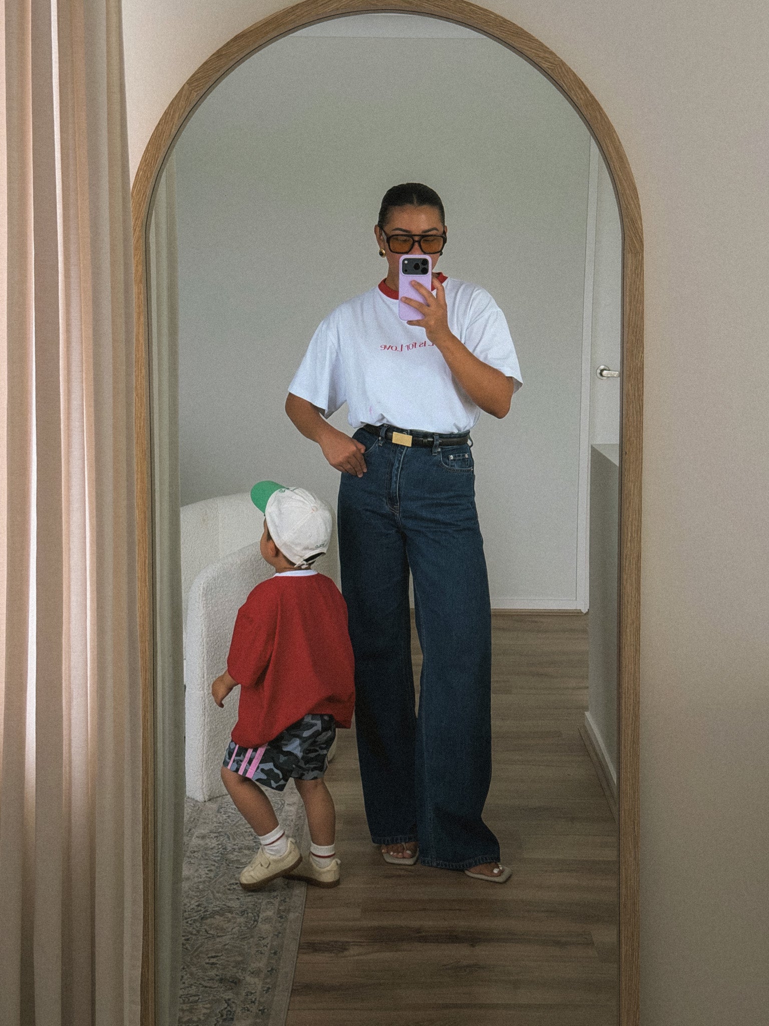 Person taking a mirror selfie with a child in a room.