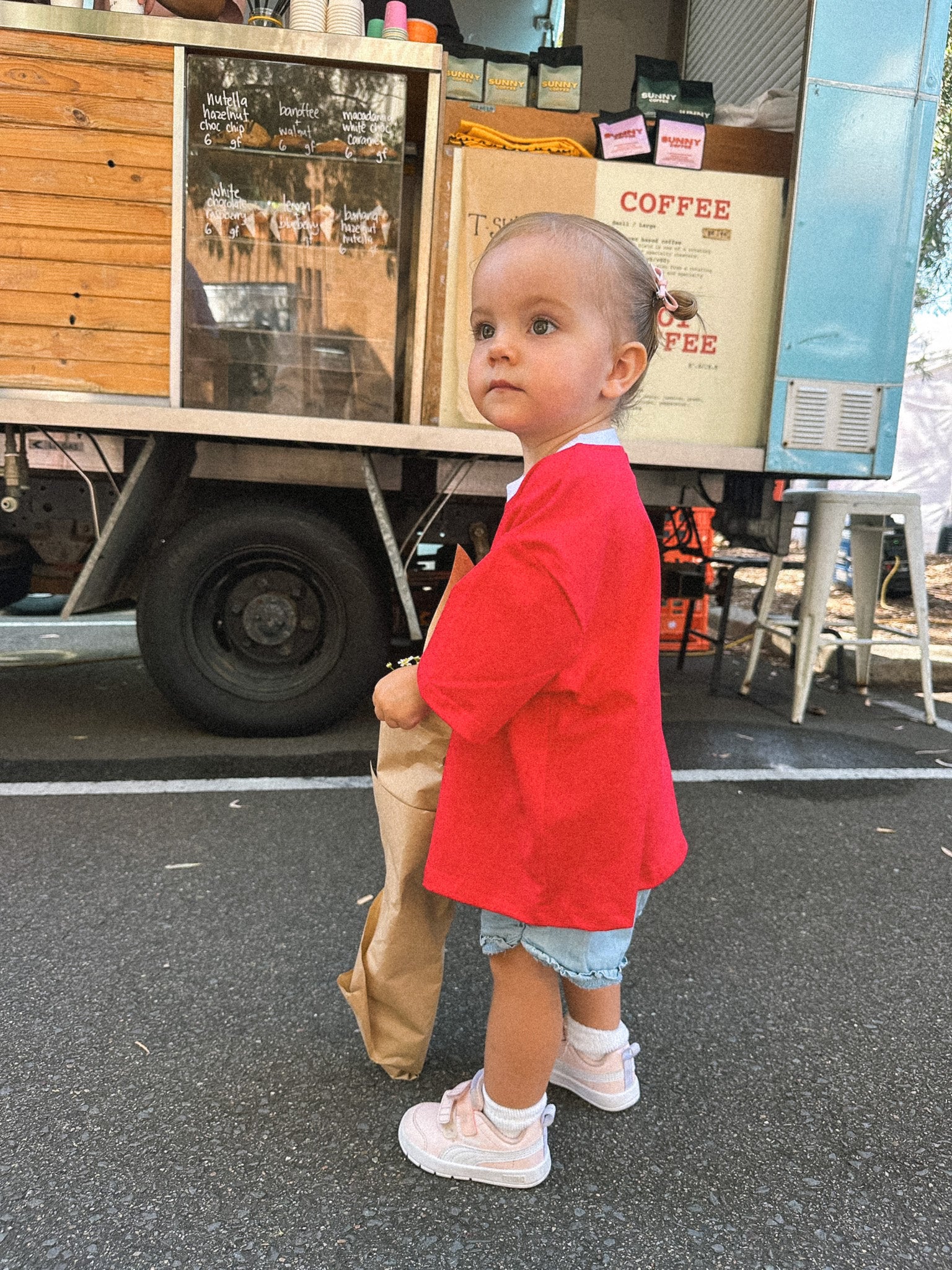 Child in a red jacket holding a paper bag in front of a coffee truck.