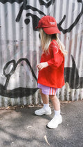 child wearing a red outfit with a cap in front of a graffiti-covered wall