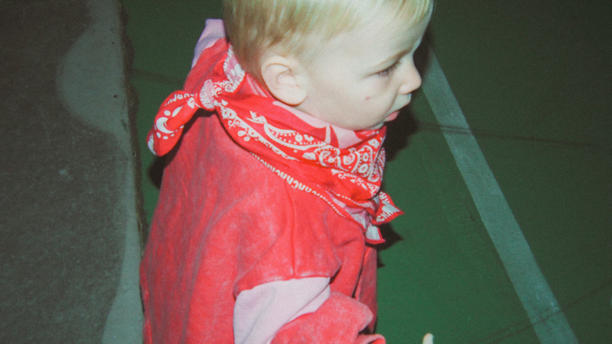 Child wearing a red bandana with white patterns on a green floor.