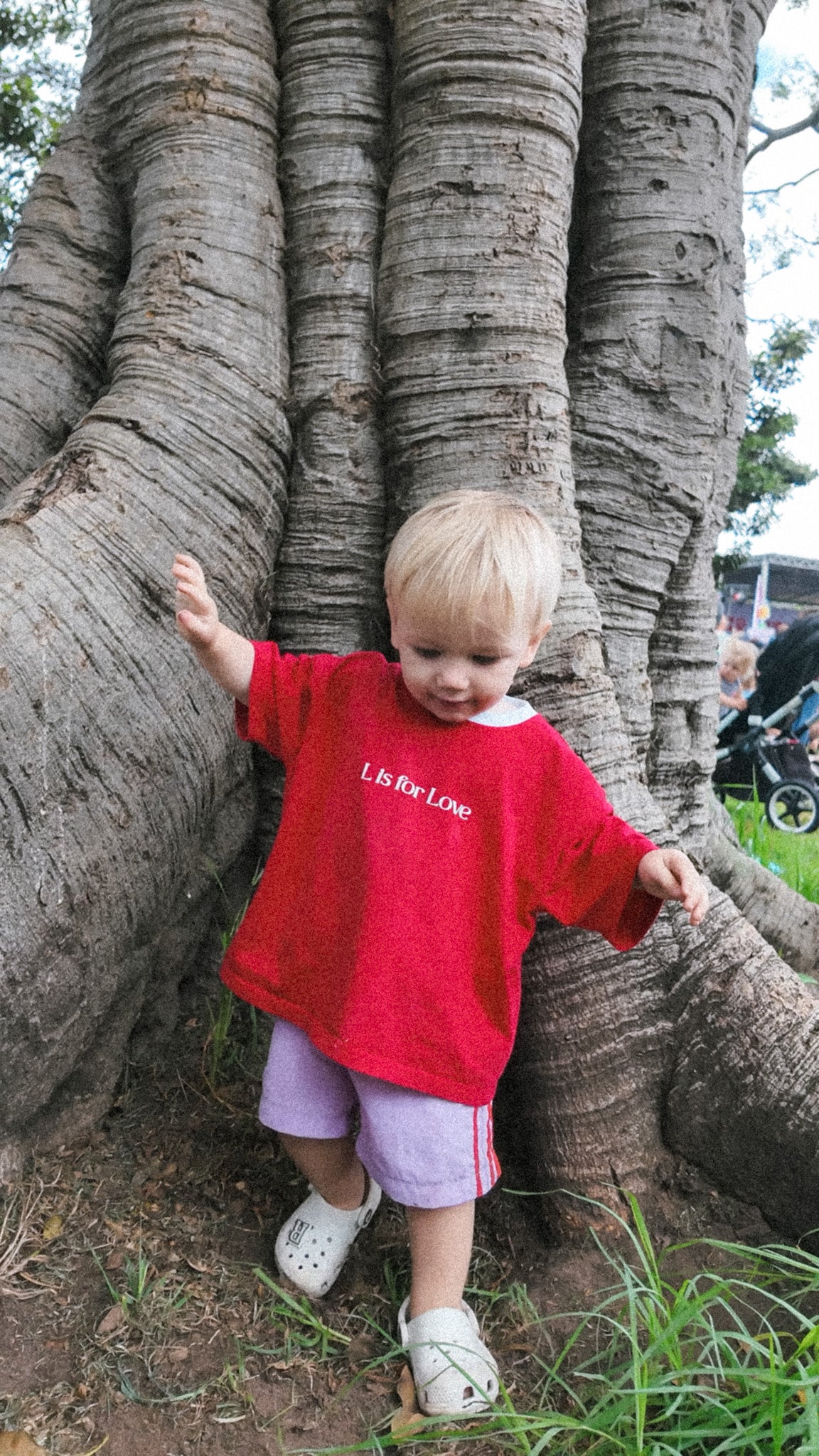 Child in a red shirt standing next to a large tree