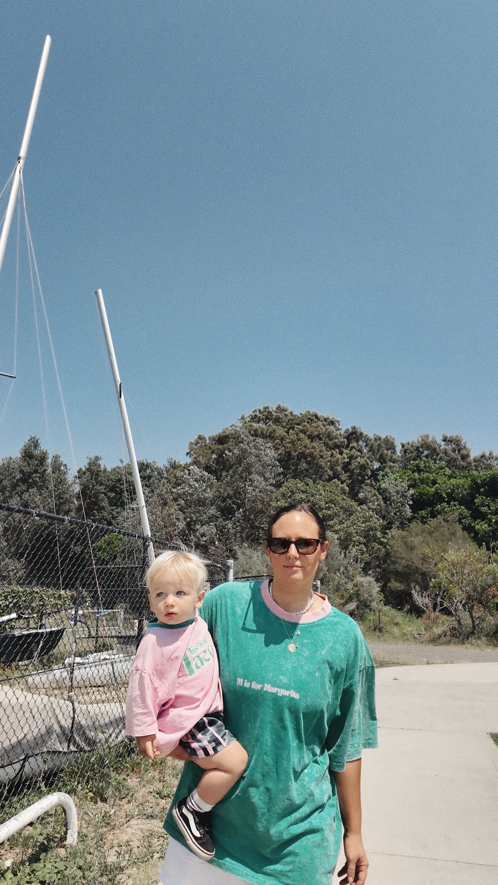 Woman in a green shirt holding a child outdoors with trees and clear sky in the background