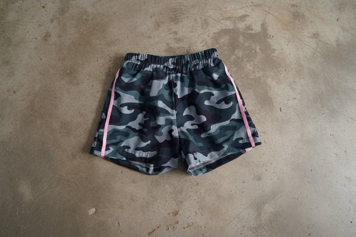 Camouflage shorts with pink accents on a concrete floor