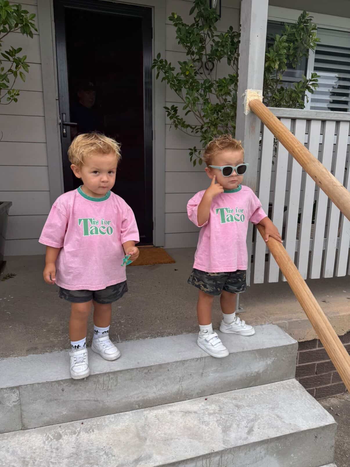 Two children in pink shirts standing on a set of stairs outside a house.