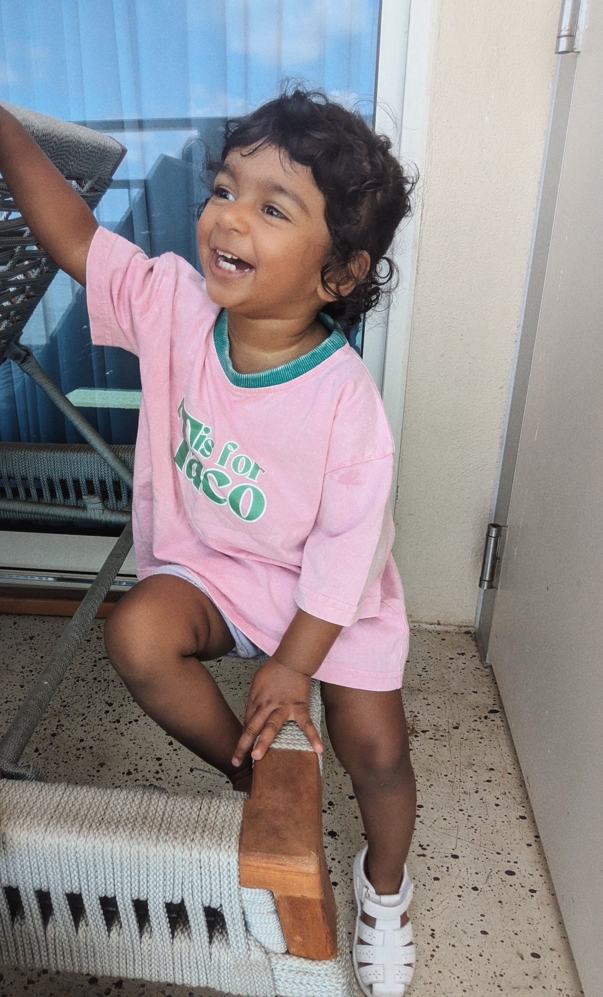 Child in a pink shirt with text sitting on a chair indoors