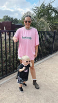 Woman in pink oversized t-shirt and sunglasses standing with a child in sunglasses outdoors.