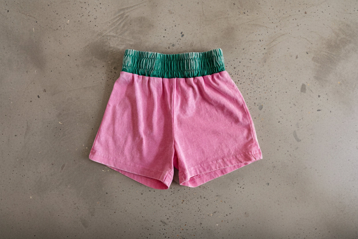 Pink shorts with green waistband on a gray surface