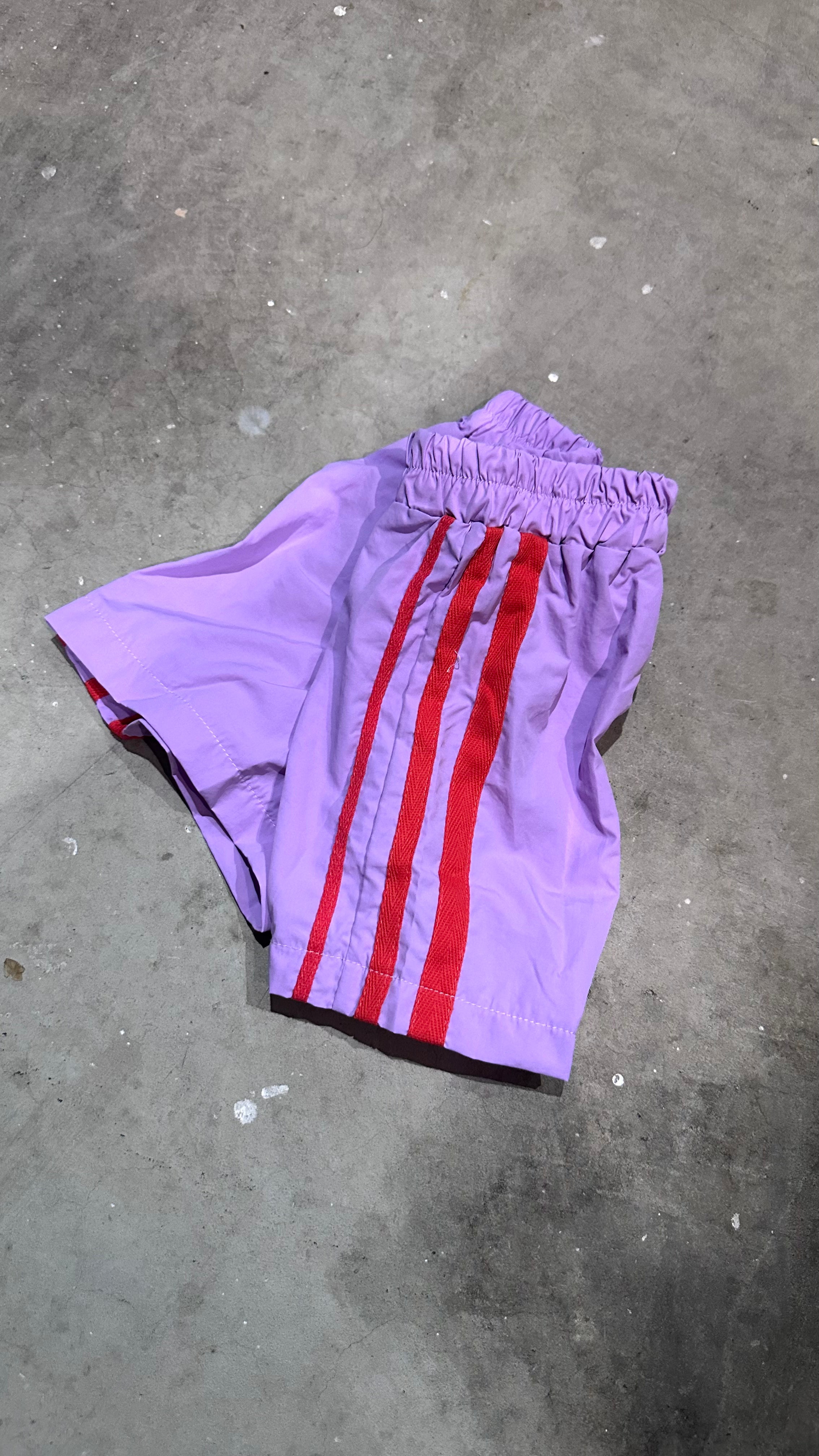 Purple shorts with red stripes on a gray concrete surface