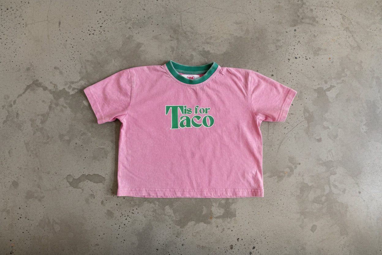 Pink t-shirt with 'Tis for Taco' text on a concrete surface