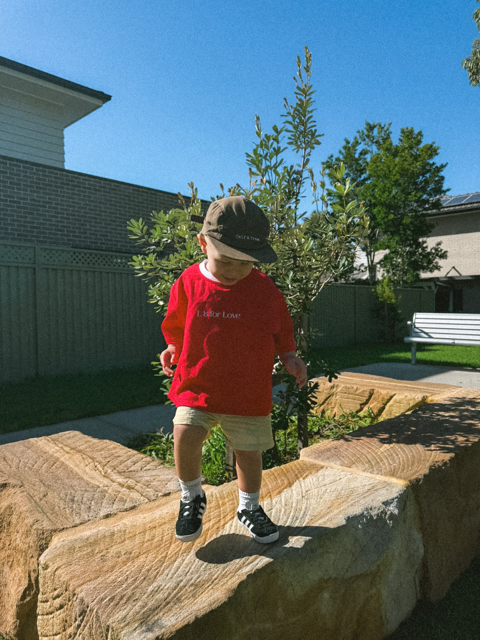 Child in a red sweatshirt and cap standing on a large stone slab outdoors.