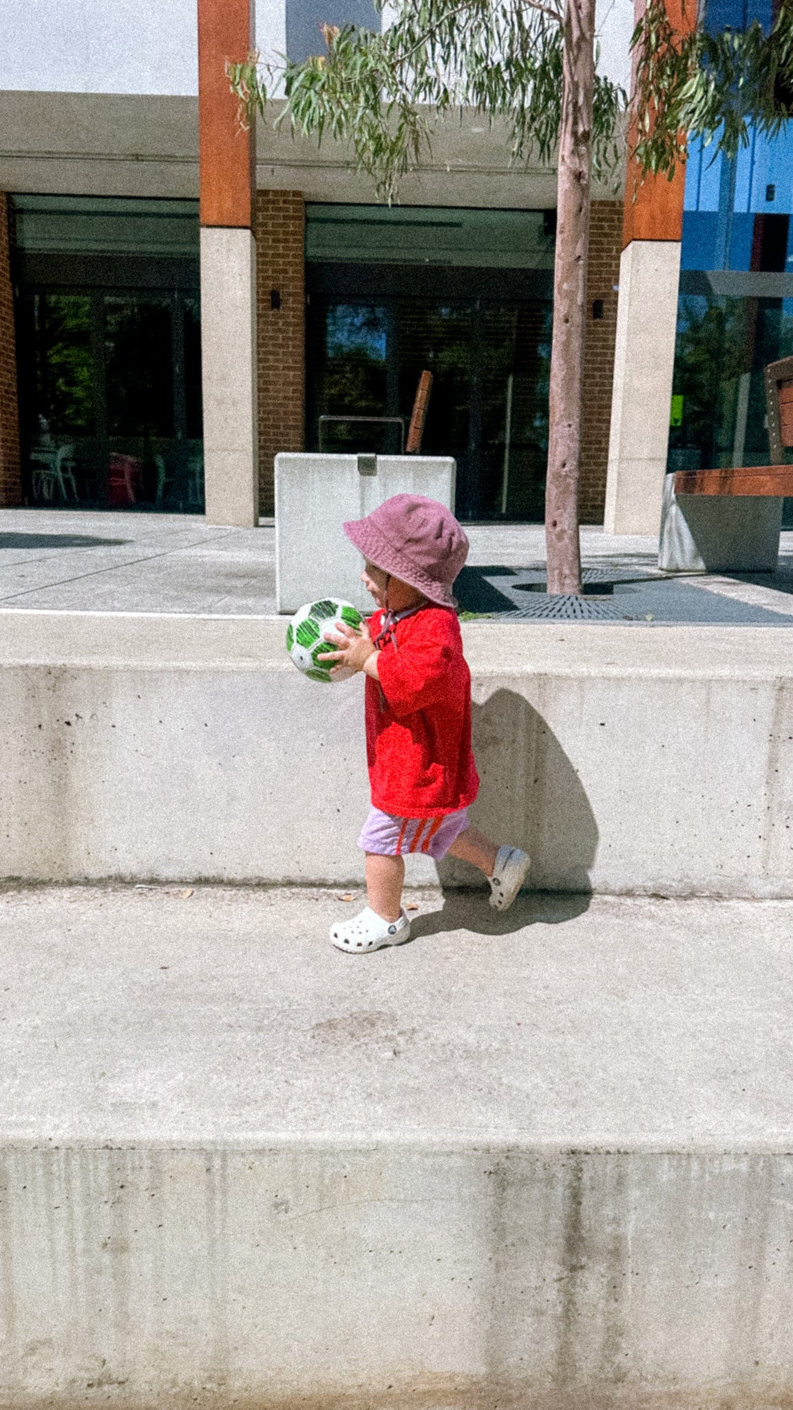 Child in a red coat and pink hat walking on concrete steps outdoors.